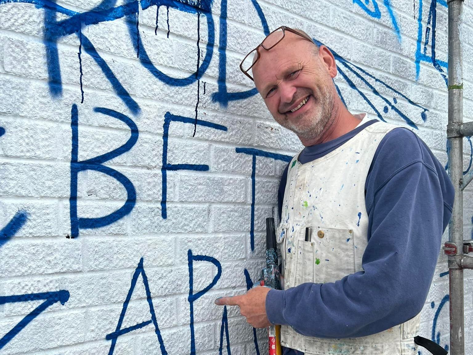 A man standing in front of a brick wall with graffiti on it