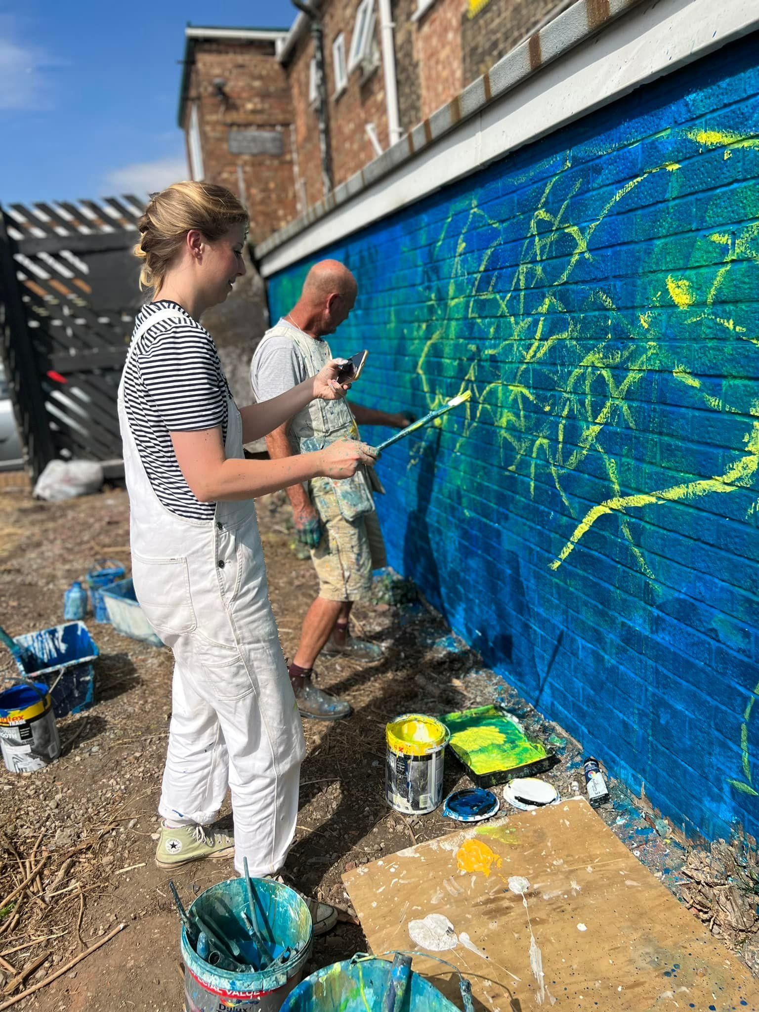 A man and a woman are painting a mural on a brick wall.