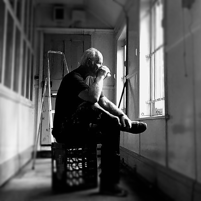 A man is sitting on a crate looking out a window.