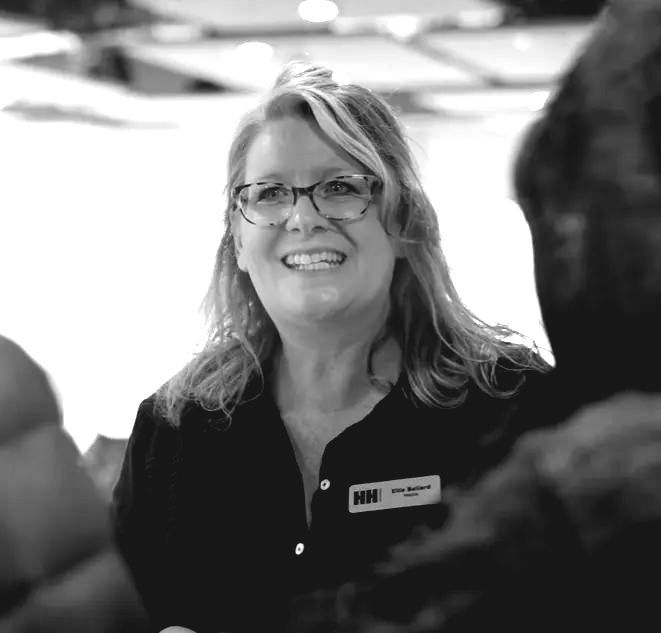 A woman wearing glasses and a name tag is smiling in a black and white photo.