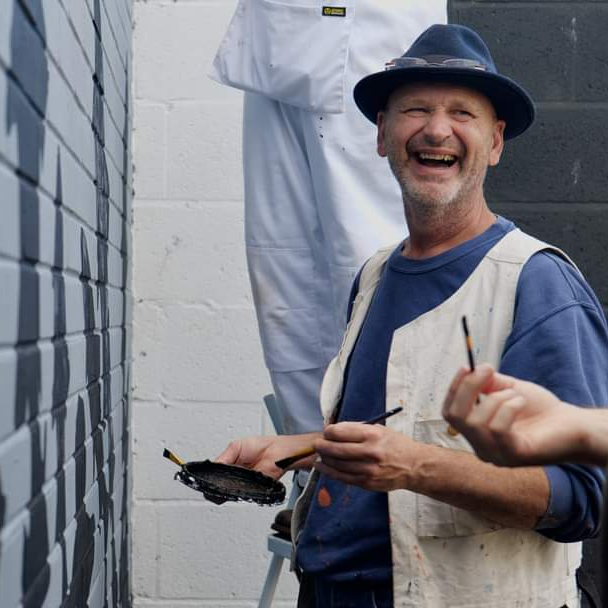 A man wearing a hat is smiling while holding a brush