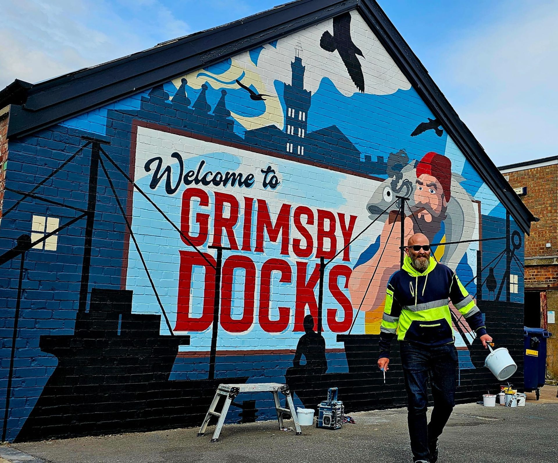 A man is walking in front of a mural that says welcome to grimsby docks