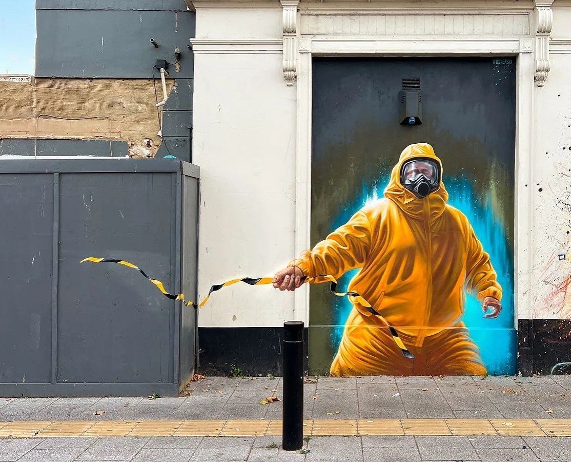 A painting of a man in a yellow suit and gas mask on a wall.