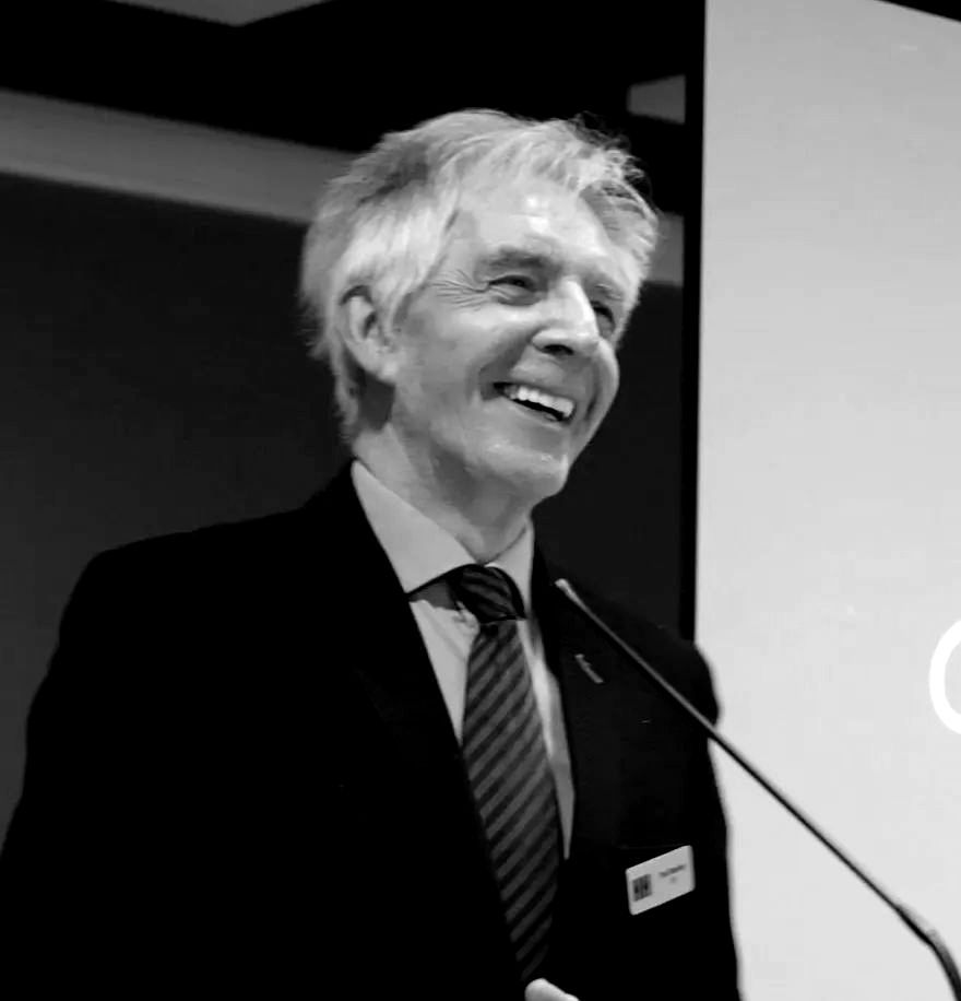 A man in a suit and tie is smiling while speaking into a microphone