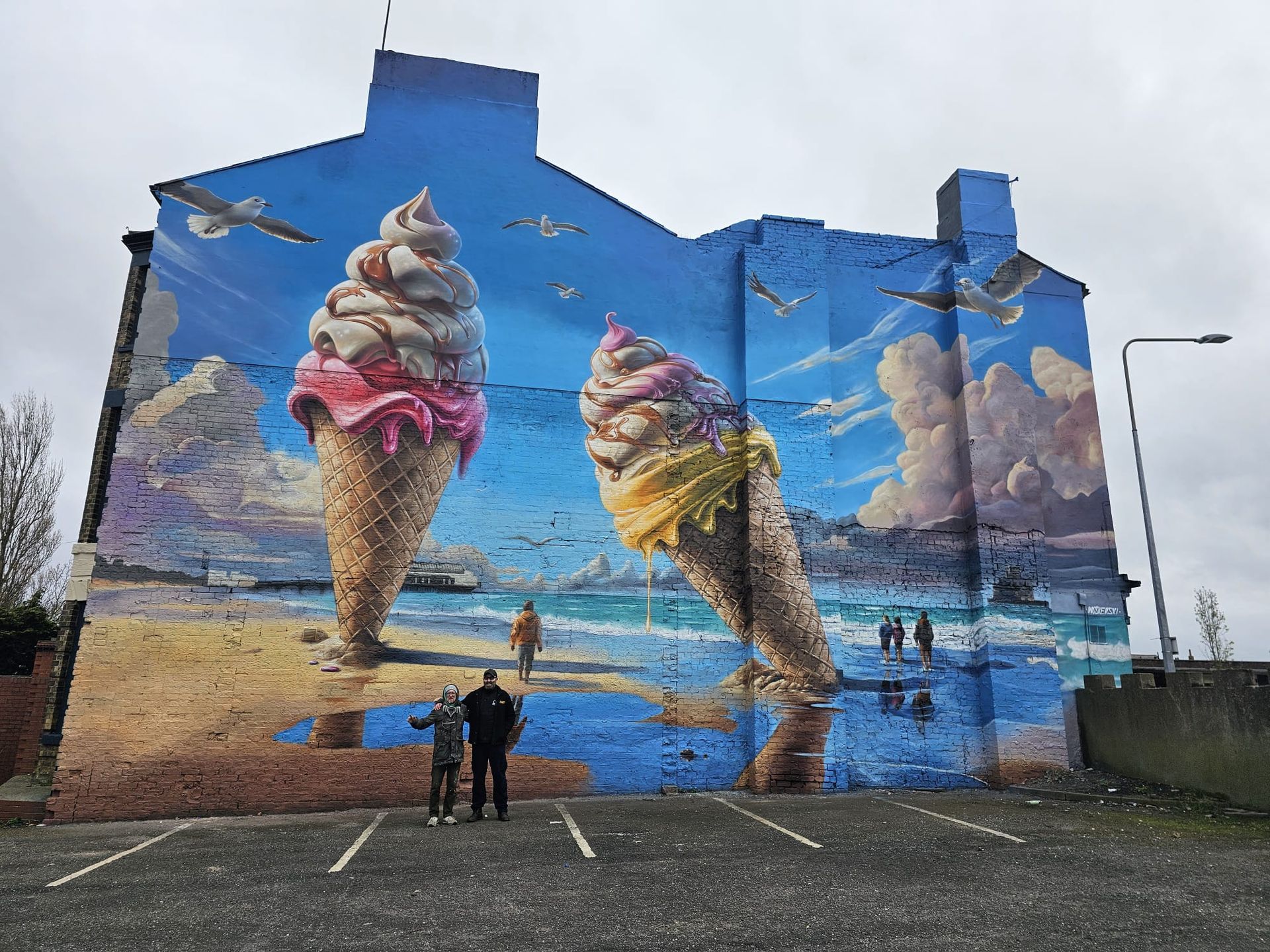 Two people are standing in front of a large mural of ice cream cones on the side of a building.