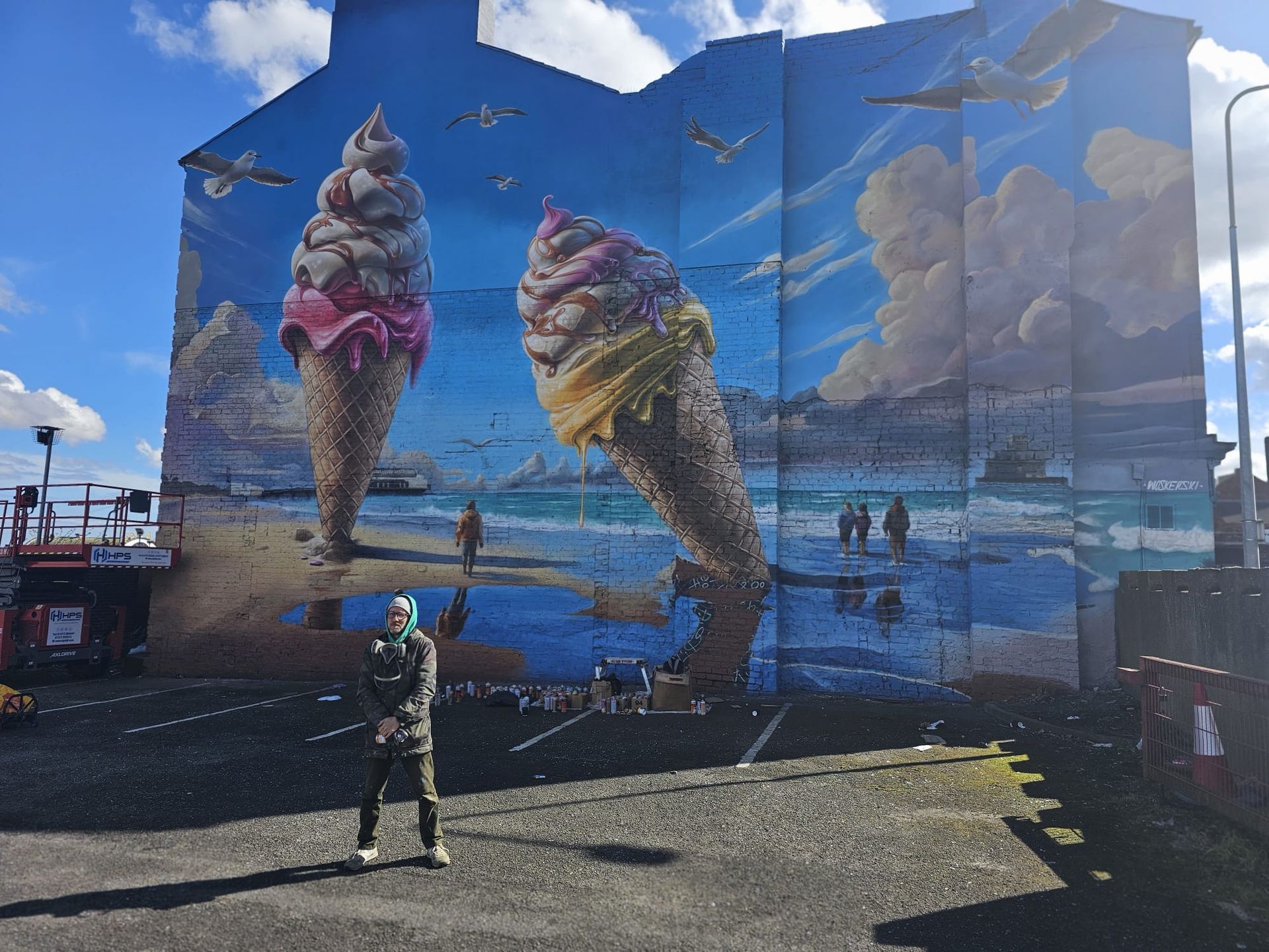A man is standing in front of a large mural of ice cream cones on the side of a building.