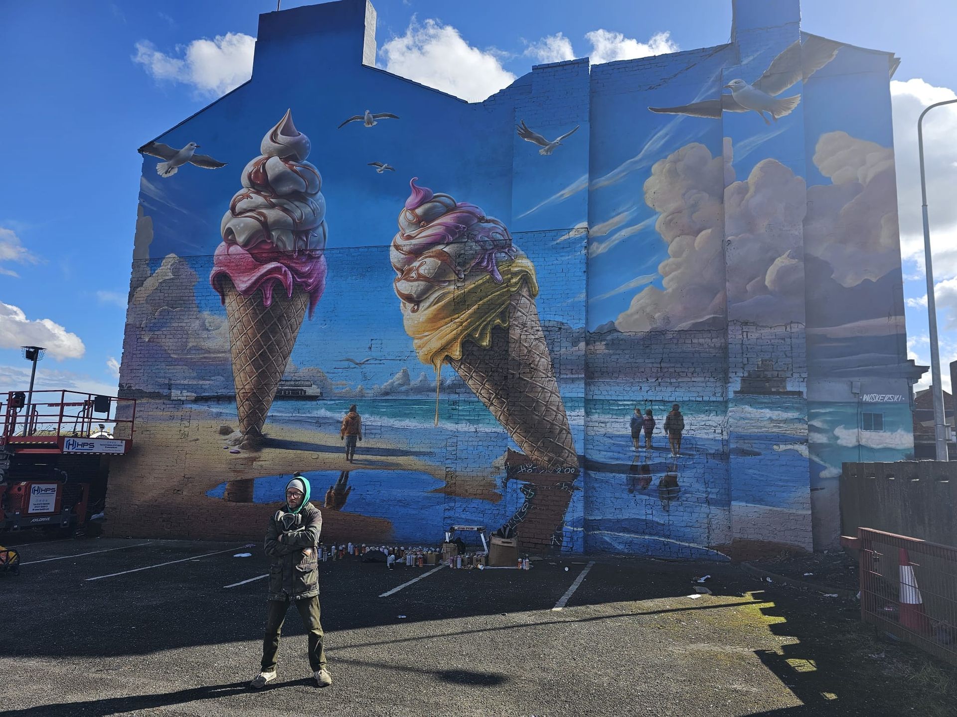 A man is standing in front of a large mural of ice cream cones on the side of a building.