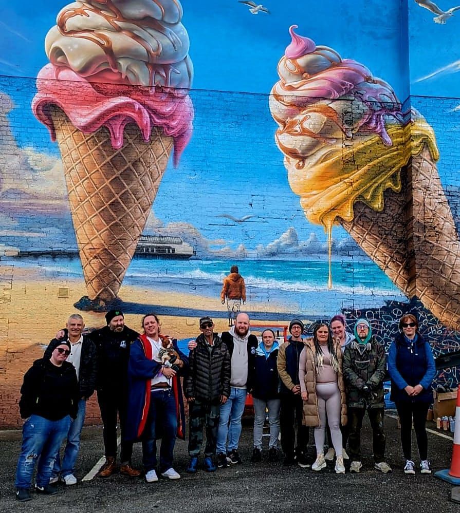 A group of people are standing in front of a mural of ice cream cones.