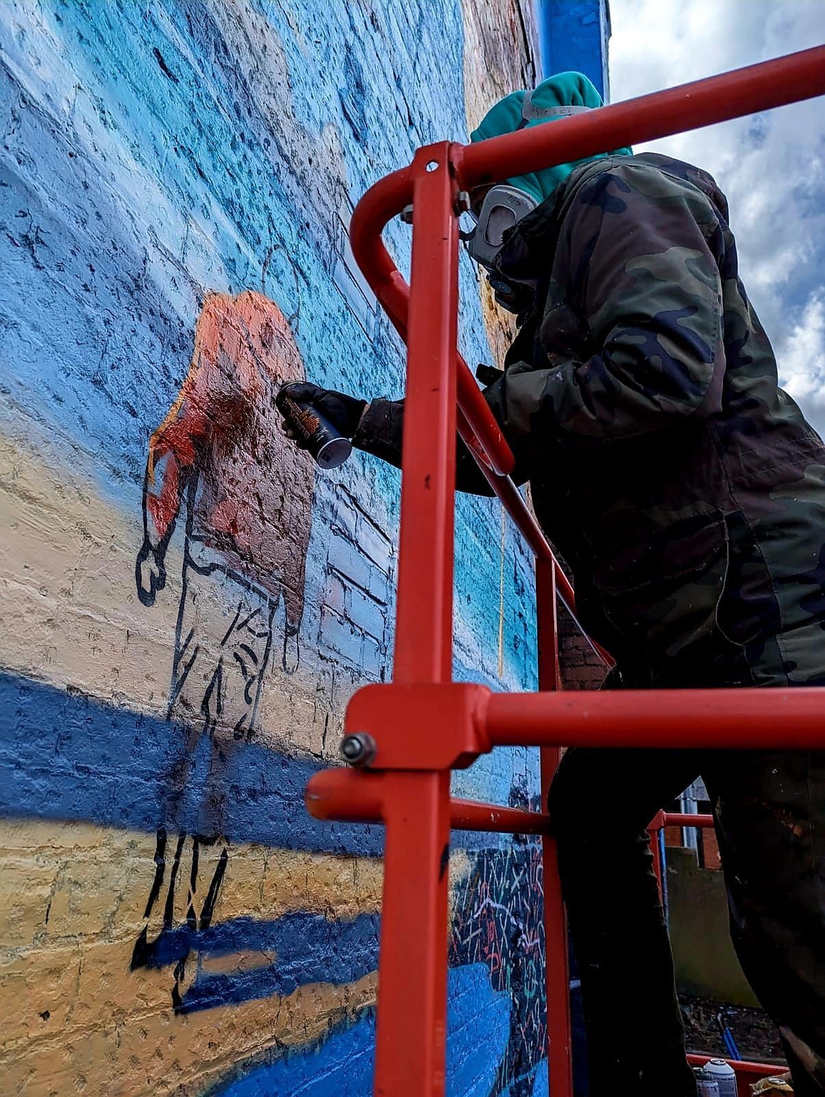 A man is painting a mural on a brick wall on a ladder.