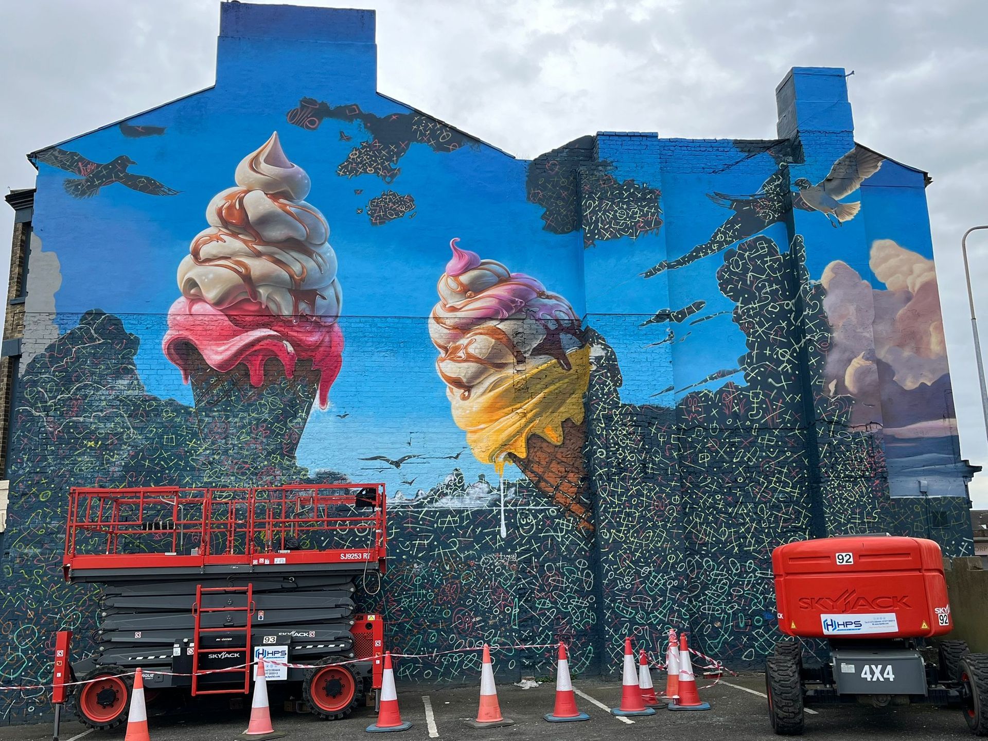 A large mural of ice cream cones is being painted on the side of a building.