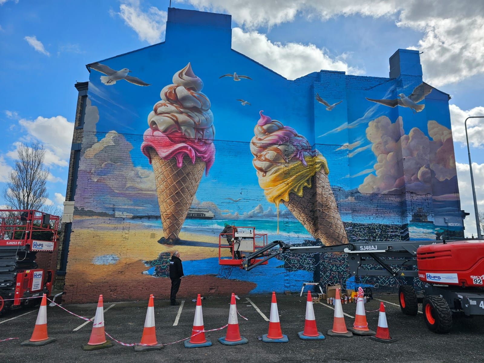 A large mural of ice cream cones is being painted on the side of a building.