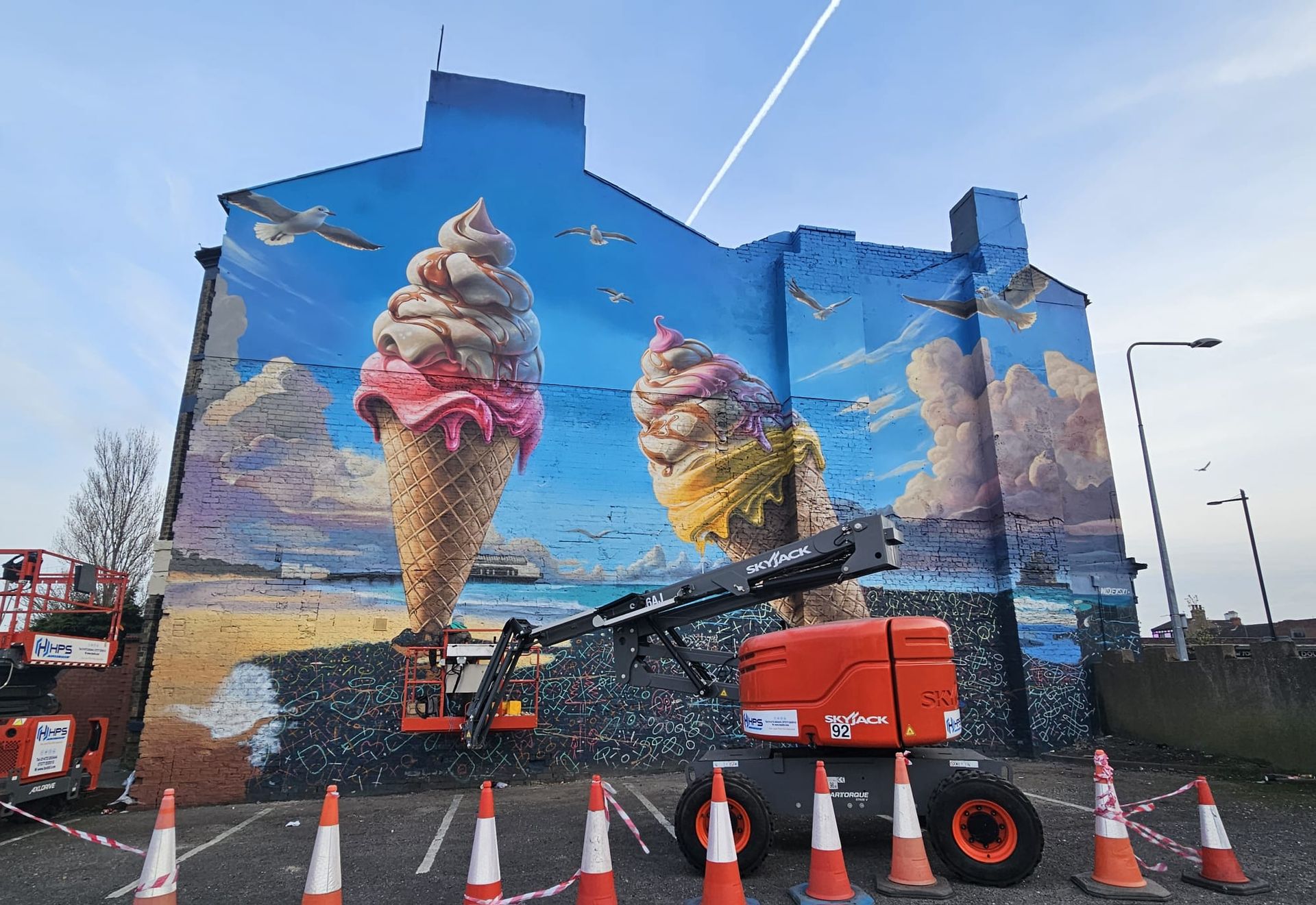 A large mural of ice cream cones is being painted on the side of a building.
