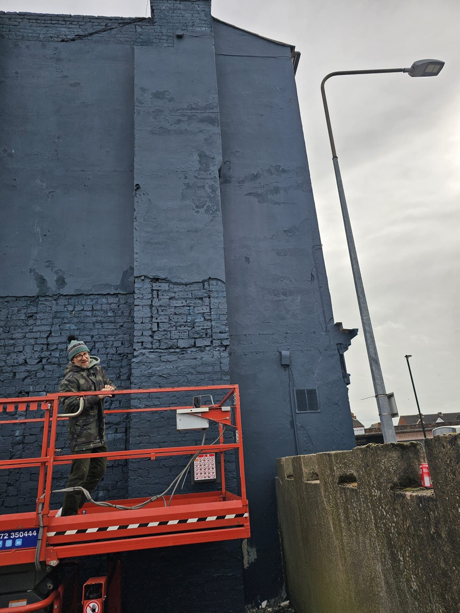 A man is standing on a lift in front of a blue building
