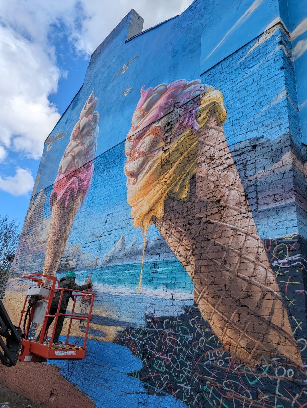A man is painting an ice cream cone on the side of a building.
