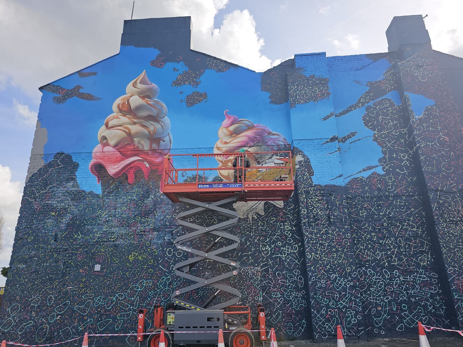 A large mural of ice cream cones is being painted on the side of a building.