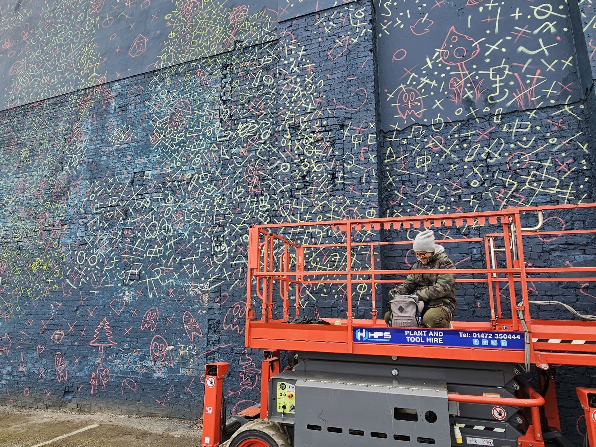A man is sitting on a lift in front of a large wall.