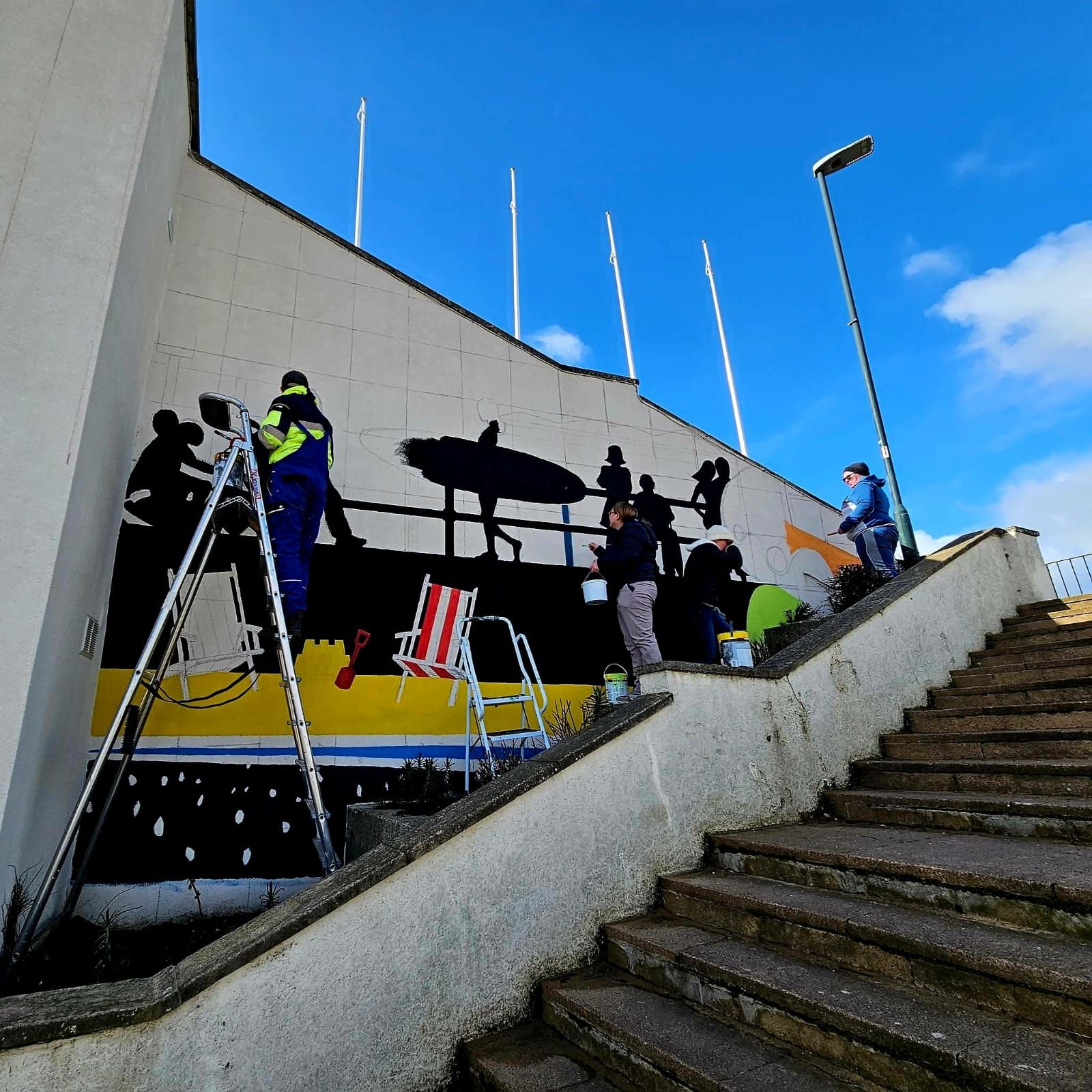 A group of people are working on a mural on the side of a building