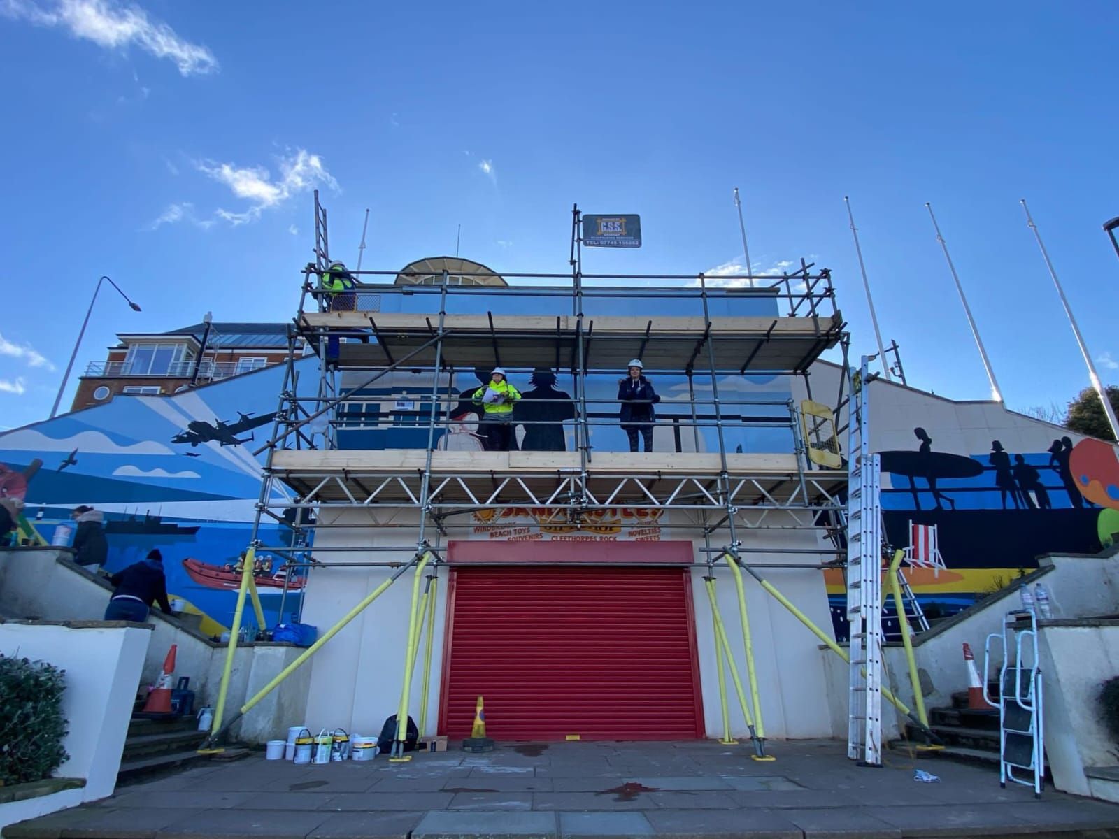 A group of people are working on a large mural on the side of a building.