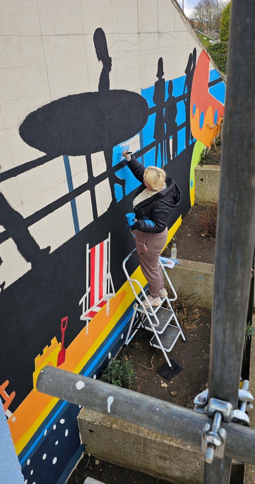 A person is standing on a ladder painting a mural on a wall.