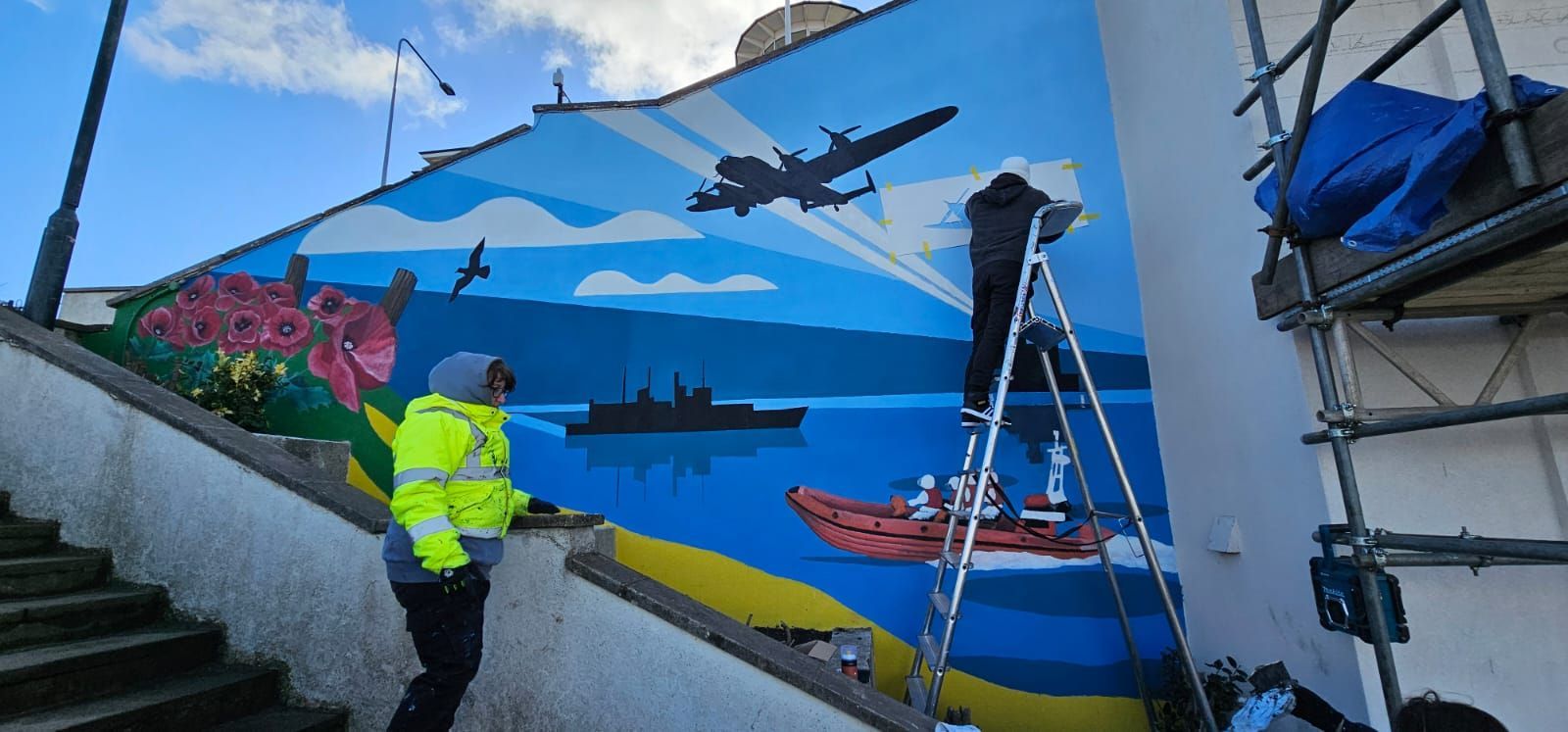 A man is painting a mural on the side of a building.