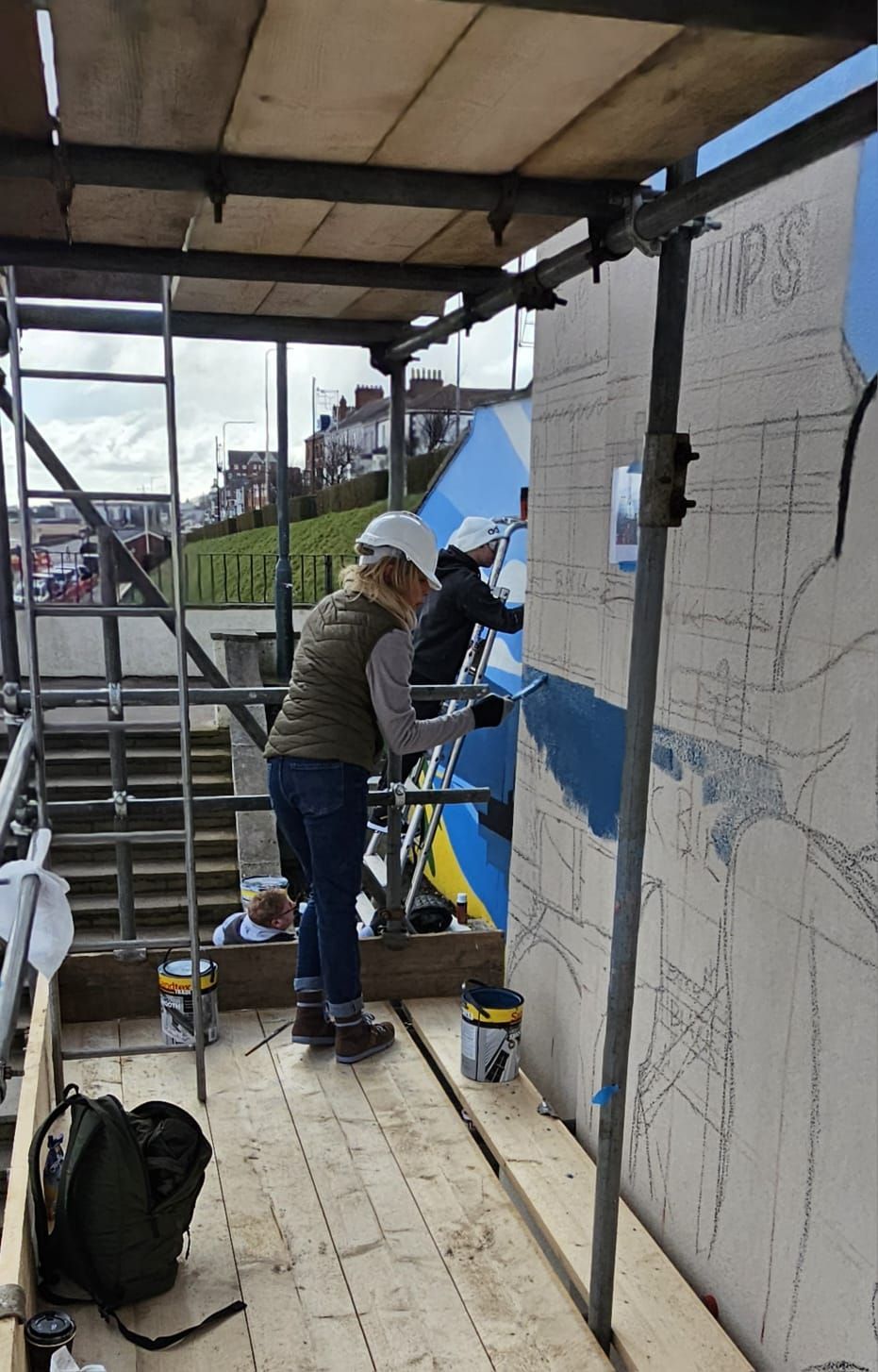 A woman is painting a wall on a scaffolding.