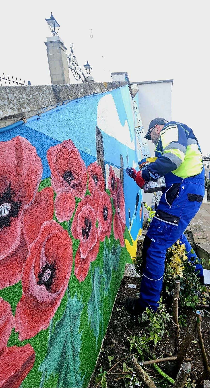 A man is painting a mural of red flowers on a wall.