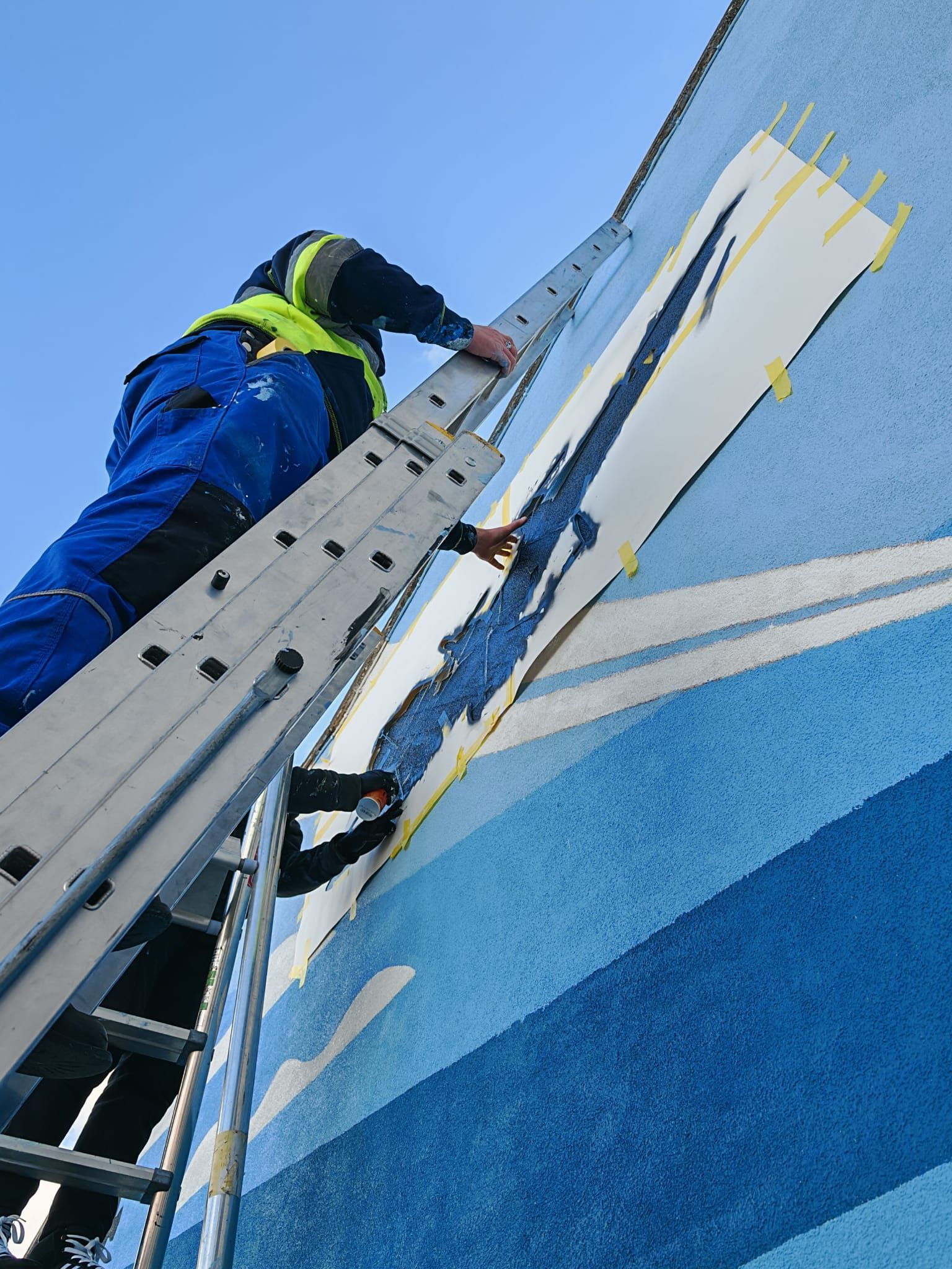A man on a ladder painting a blue and white wall