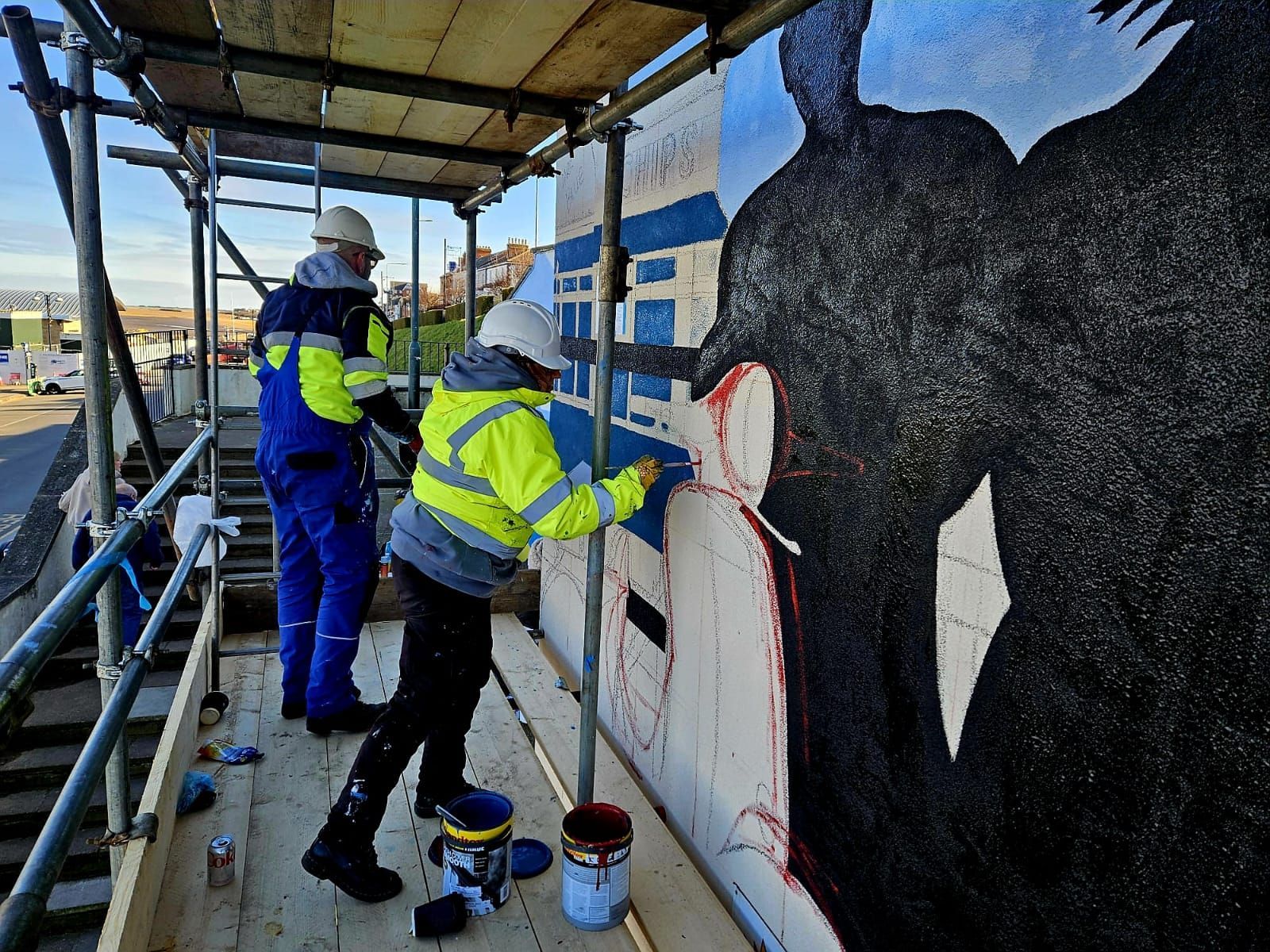 Two people are painting a mural on a scaffolding