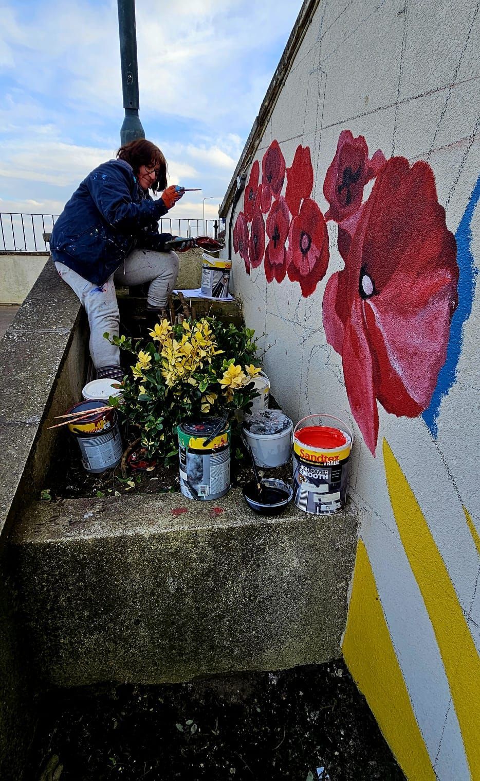 A woman is painting flowers on a wall.