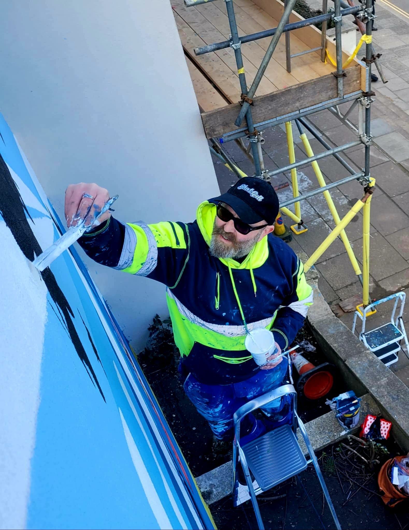 A man is standing on a ladder painting a wall.