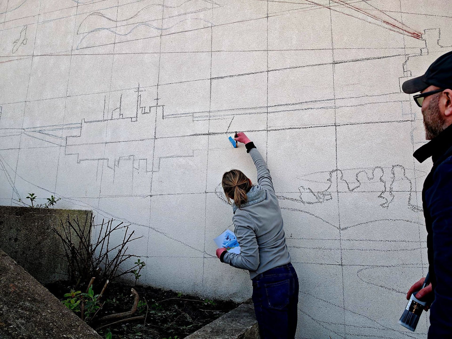 A man and a woman are cleaning a wall with a sponge.