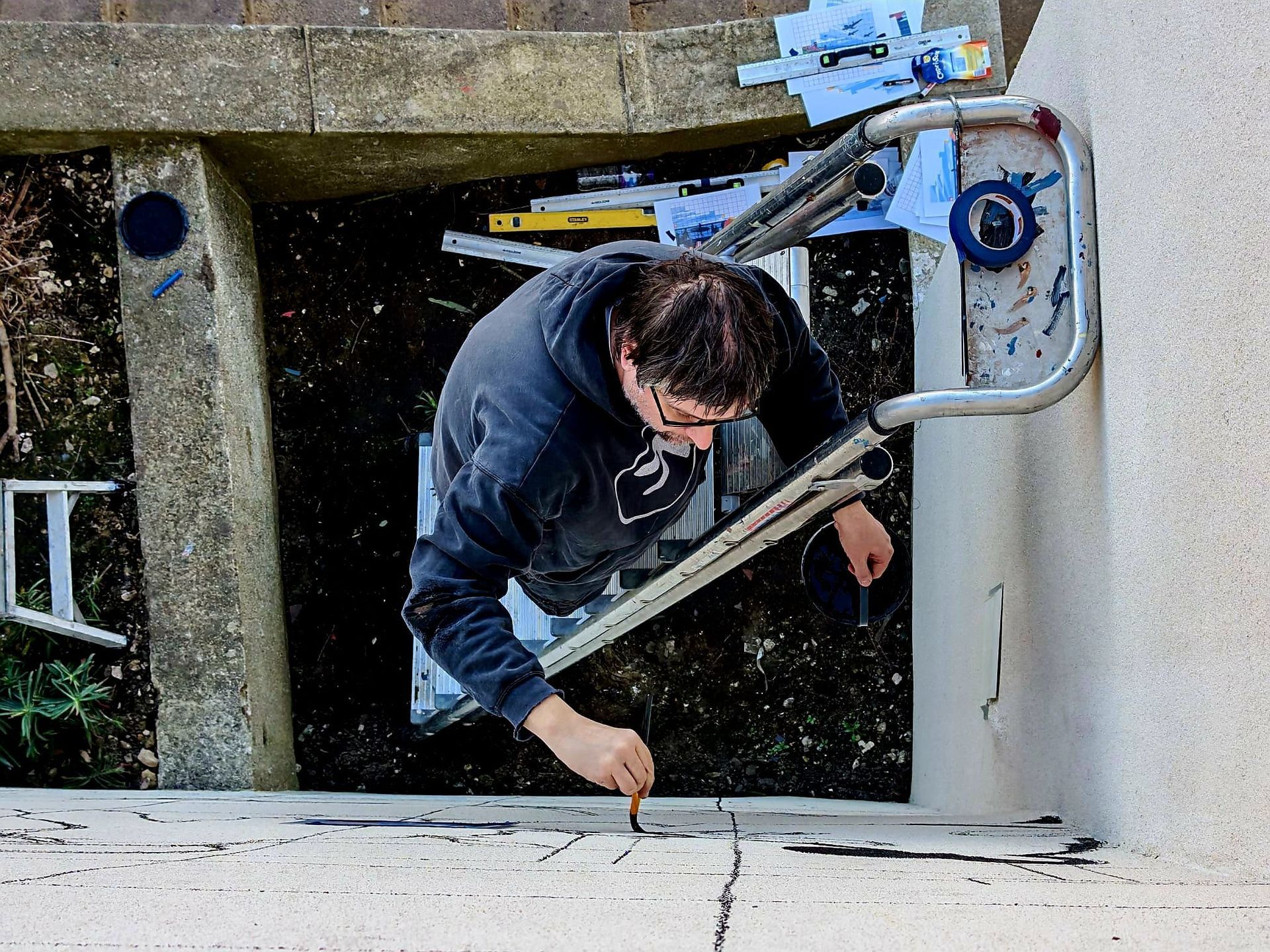 A man in a black hoodie is working on a ladder