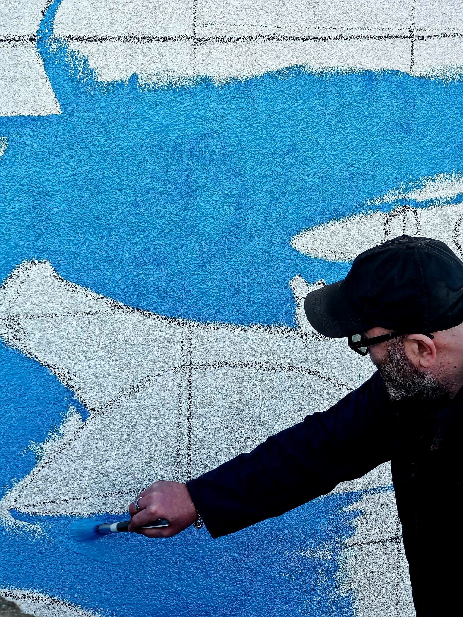 A man is painting a blue and white mural on a wall.
