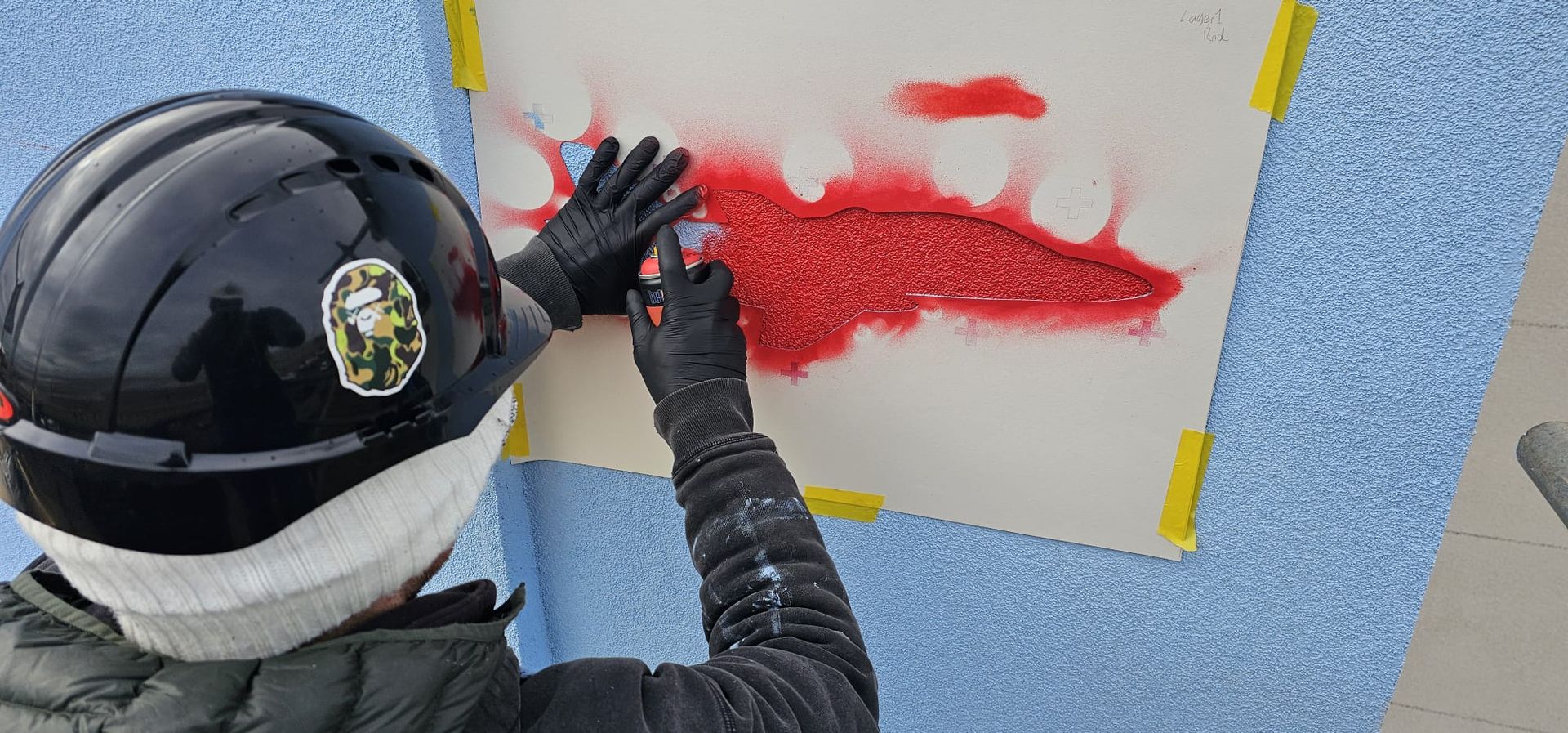 A person wearing a helmet and gloves is spray painting a picture on a wall.