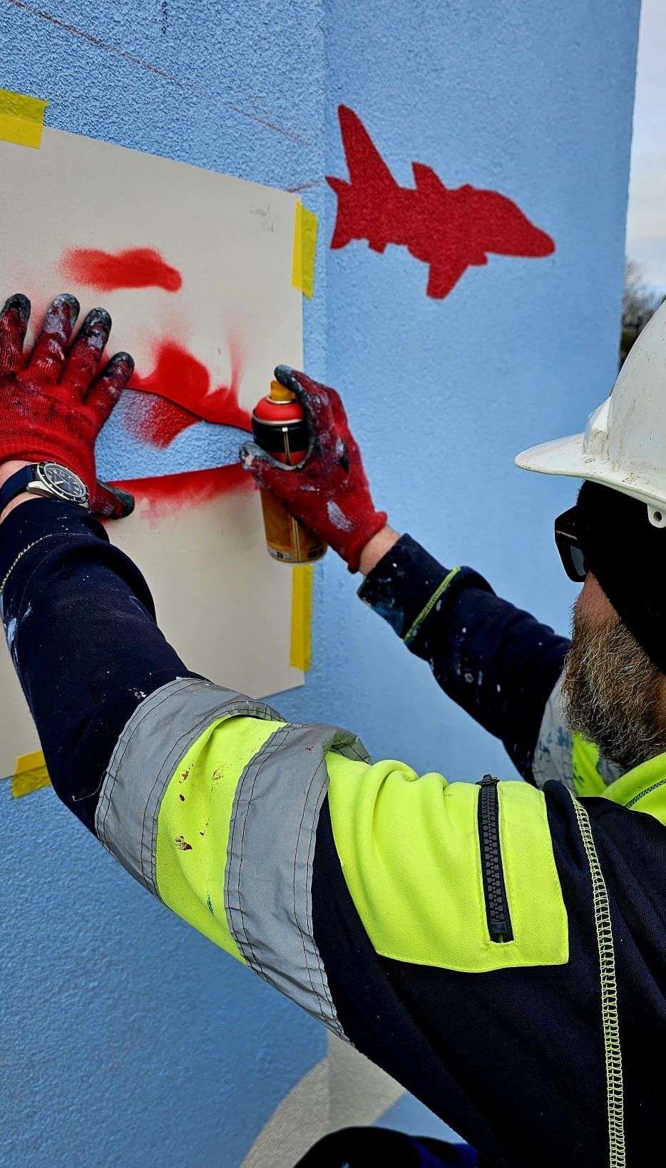A man is spray painting a fish on a wall