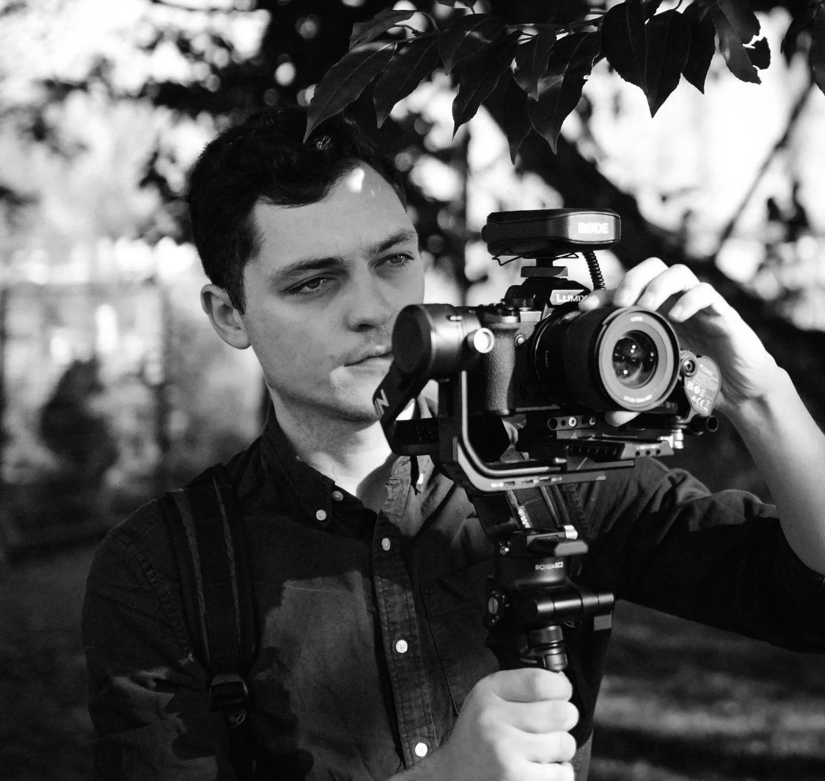 A black and white photo of a man holding a camera on a tripod