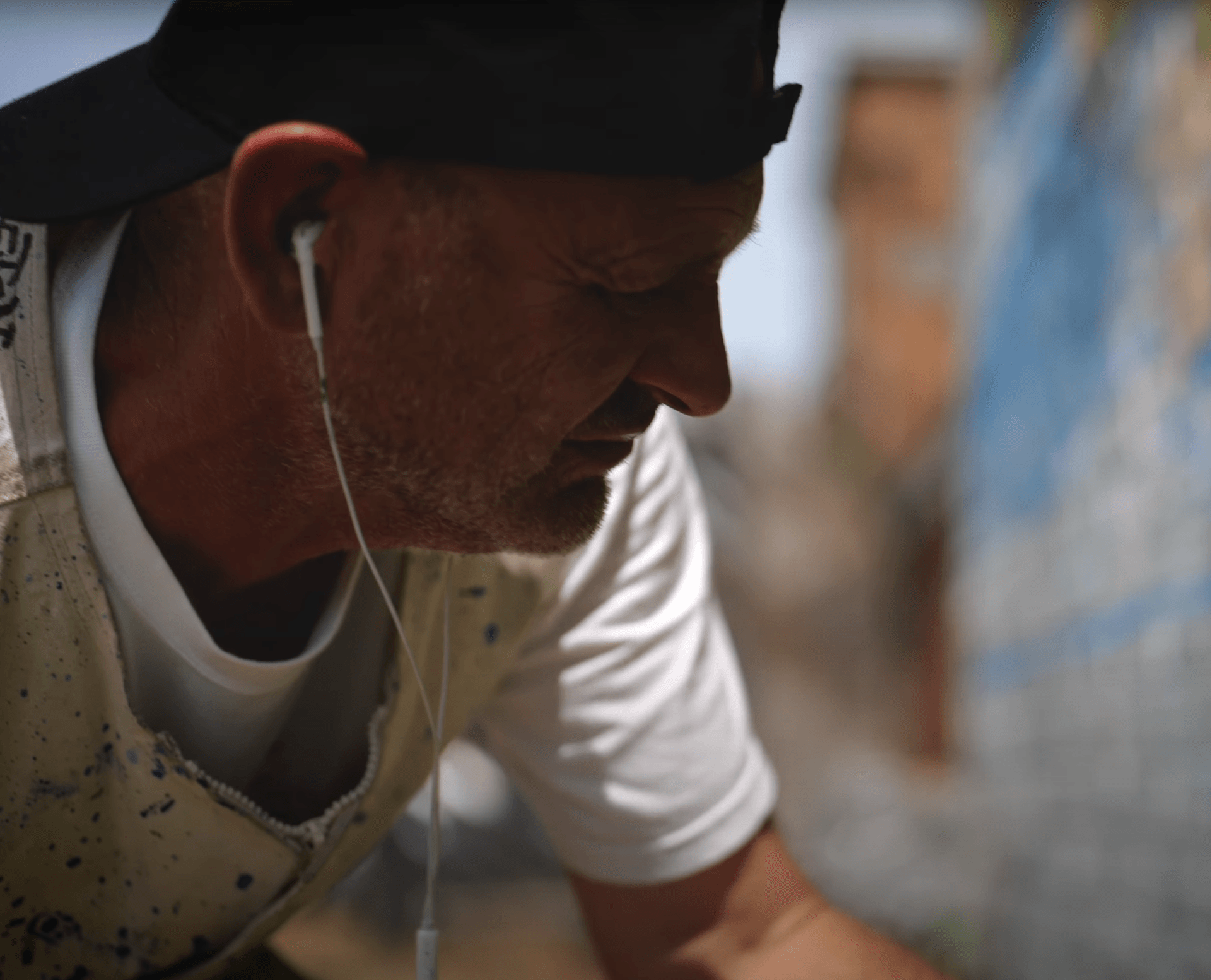 A man wearing a hat and ear buds looks down