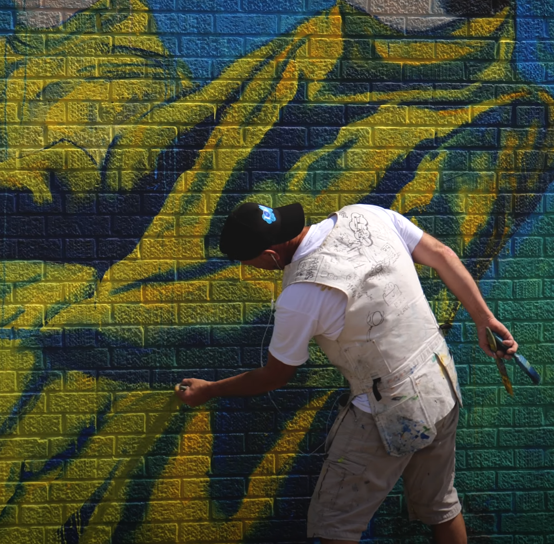 A man is painting a mural on a brick wall