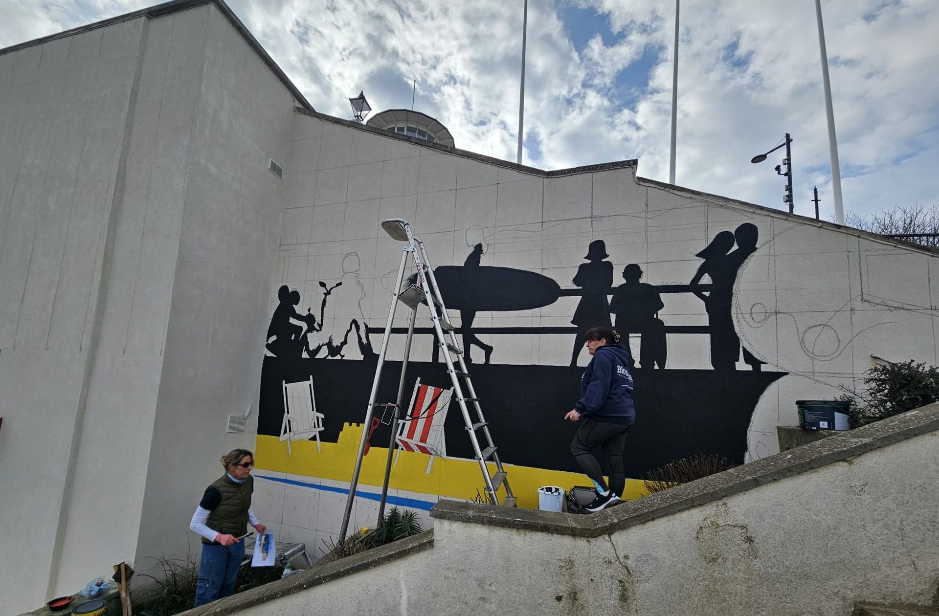 A group of people are working on a mural on the side of a building