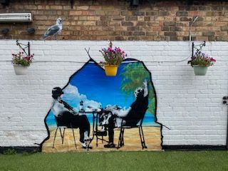 A painting of two people sitting at a table on a brick wall.