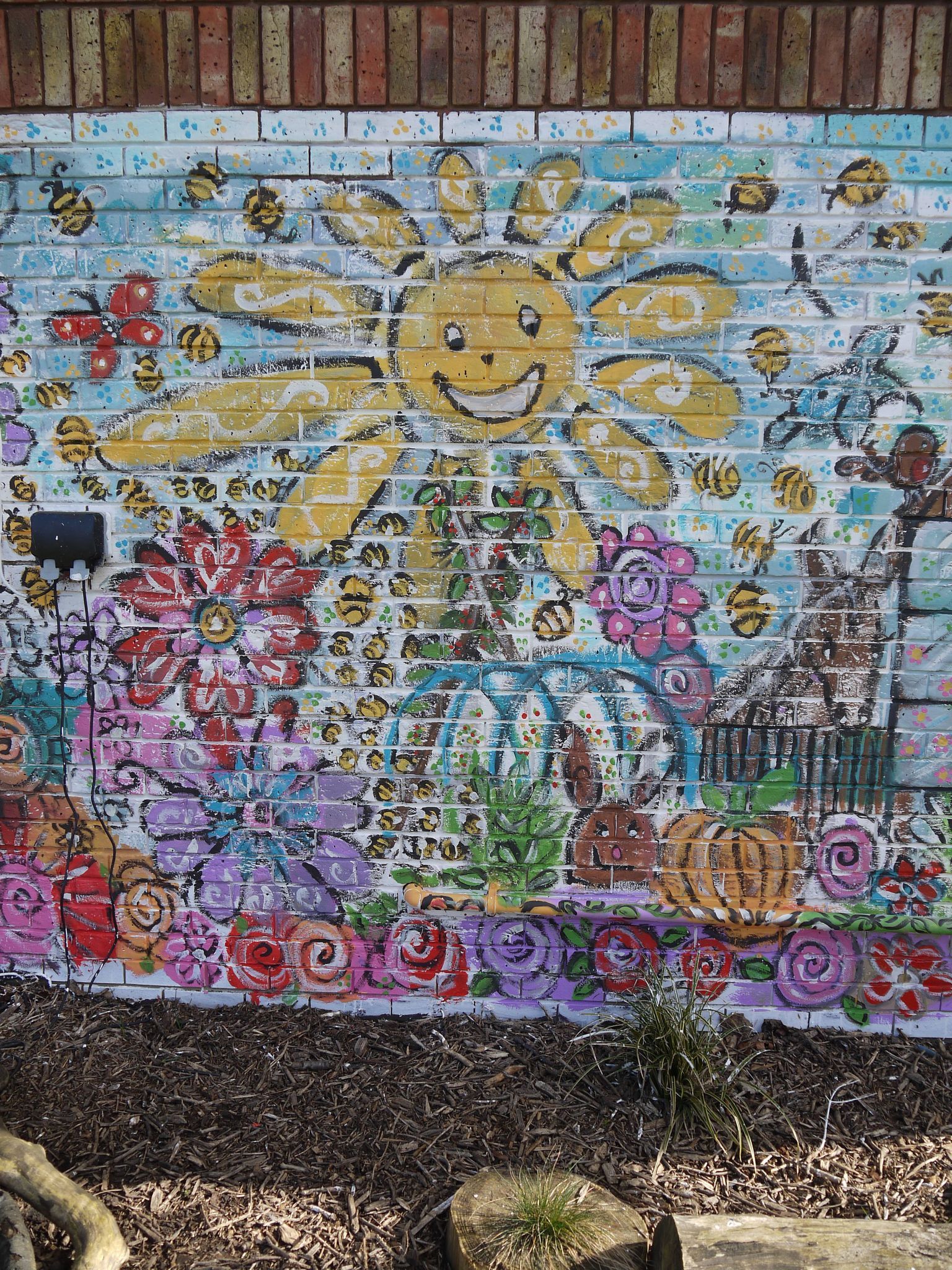 A brick wall with a mural of a sun and flowers on it.