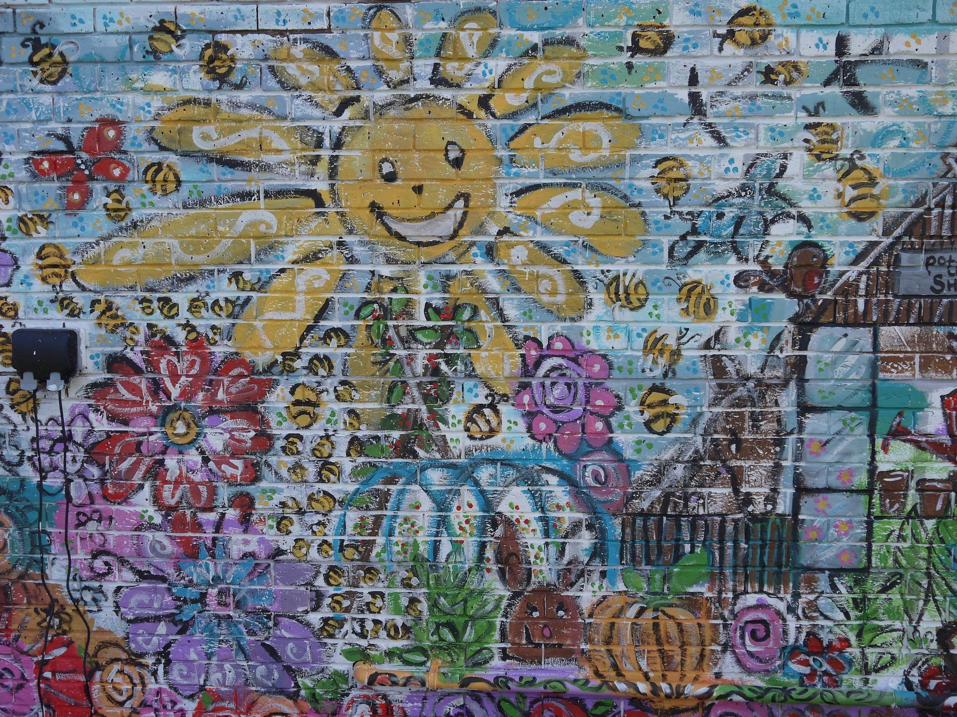 A brick wall with a painting of a sun and flowers on it.