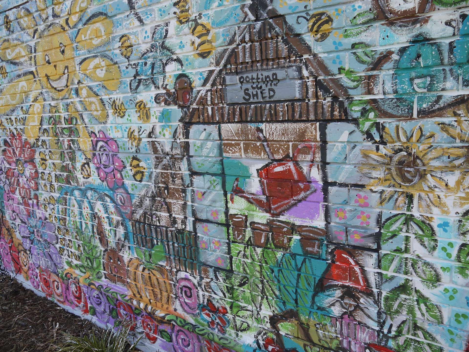 A brick wall with a painting of a greenhouse and flowers on it.