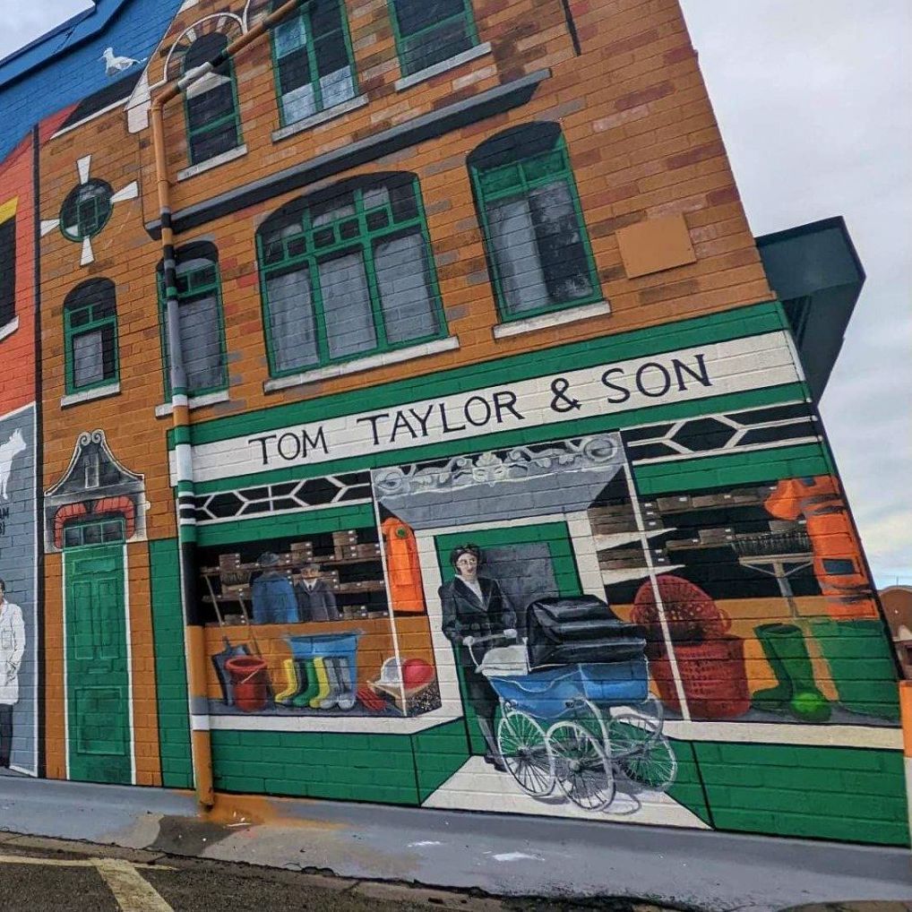 A large mural on the side of a building that says tom taylor & son