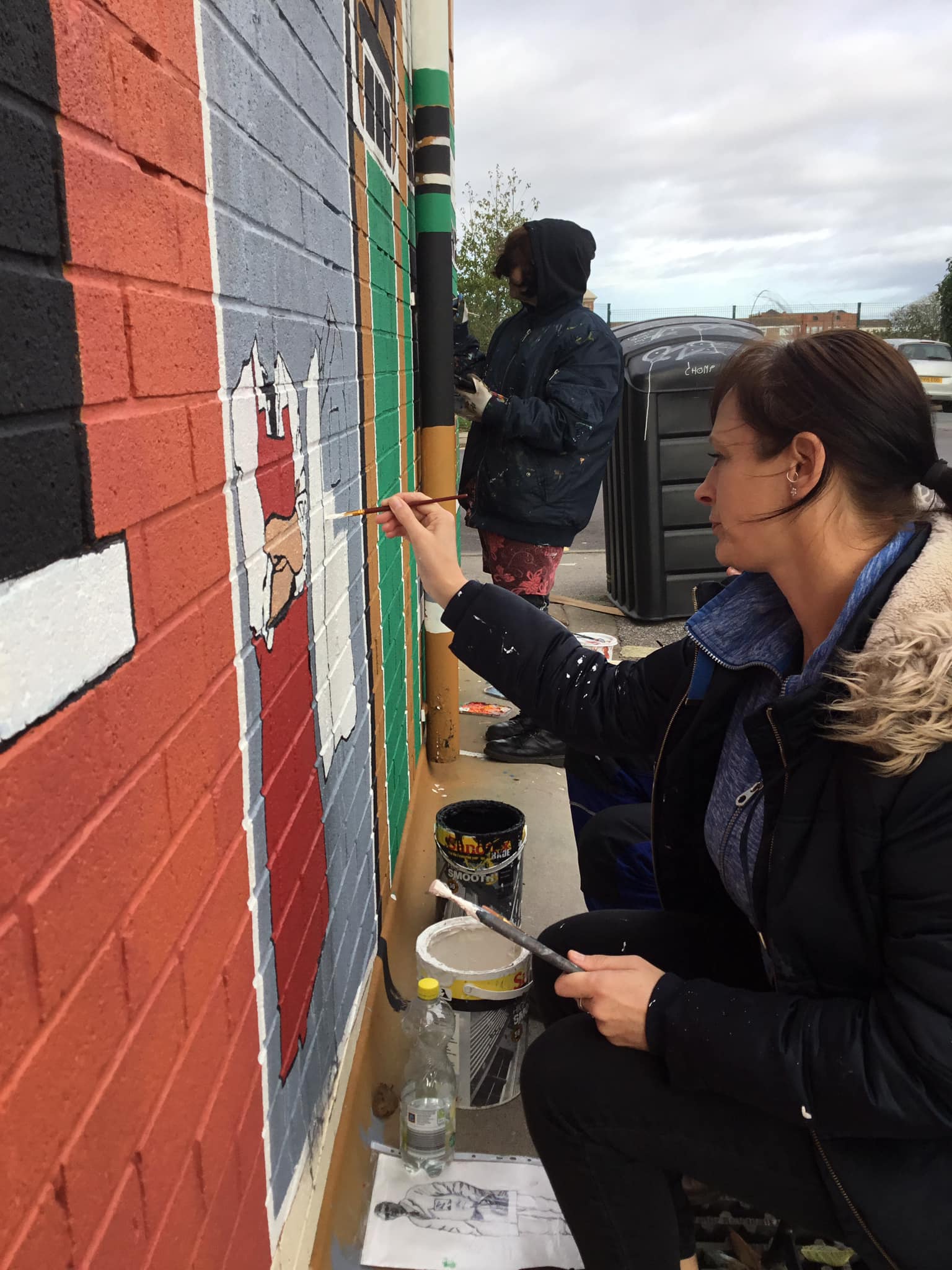 A woman is painting a picture of santa on a brick wall.