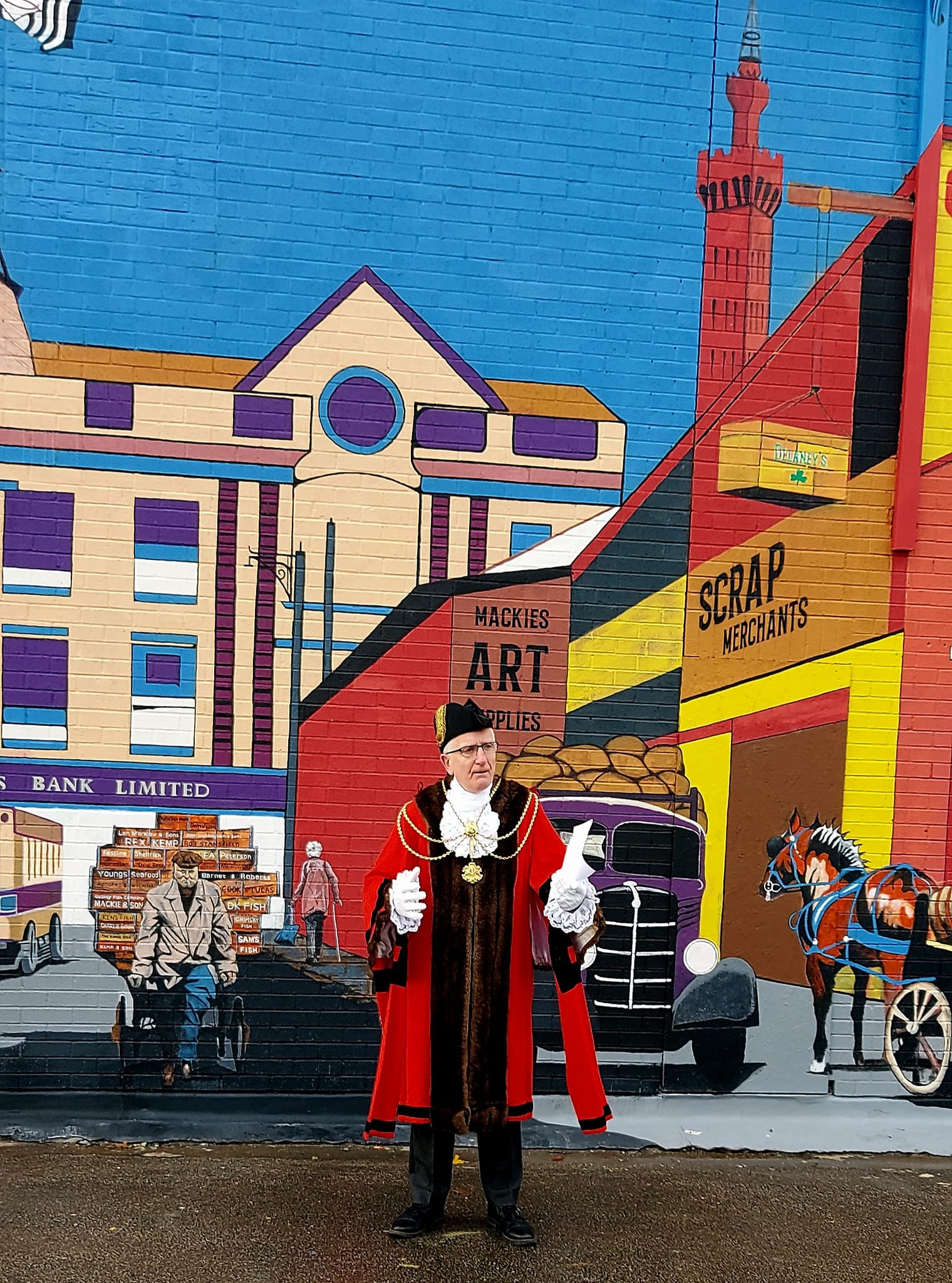 A man in a red coat is standing in front of a large mural.