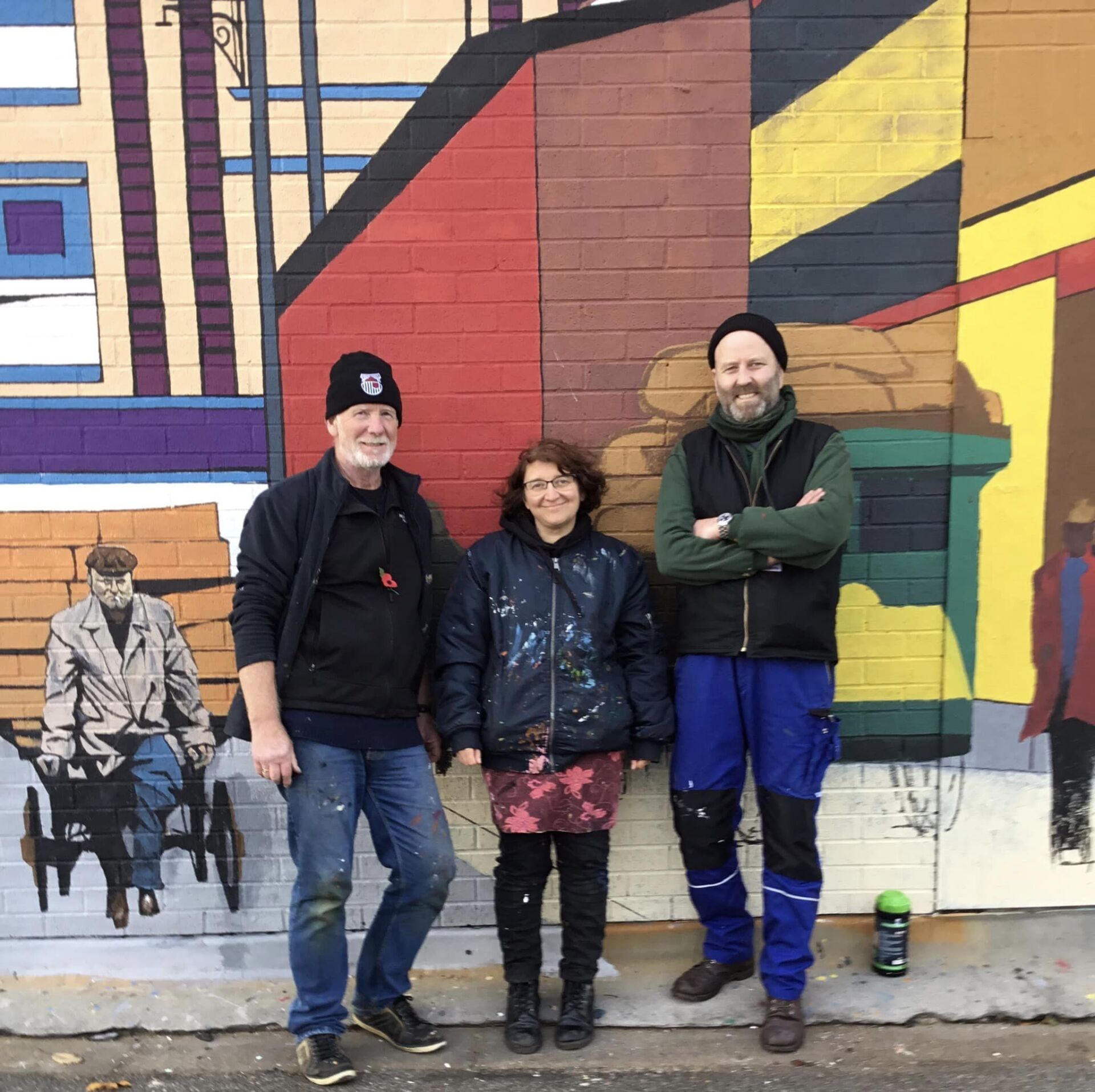 Three people are standing in front of a mural on a wall