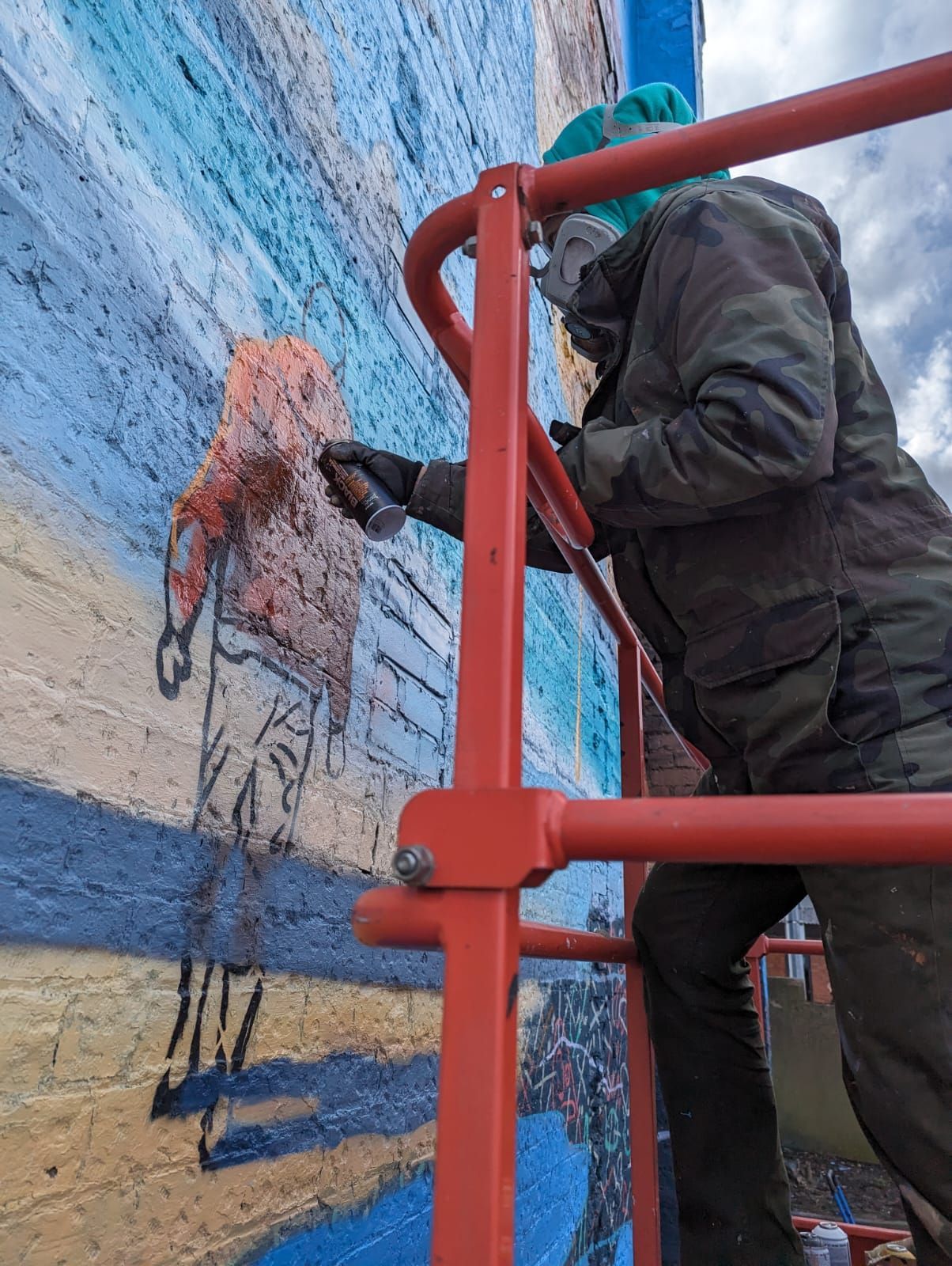 A man is painting a mural on a brick wall on a ladder.