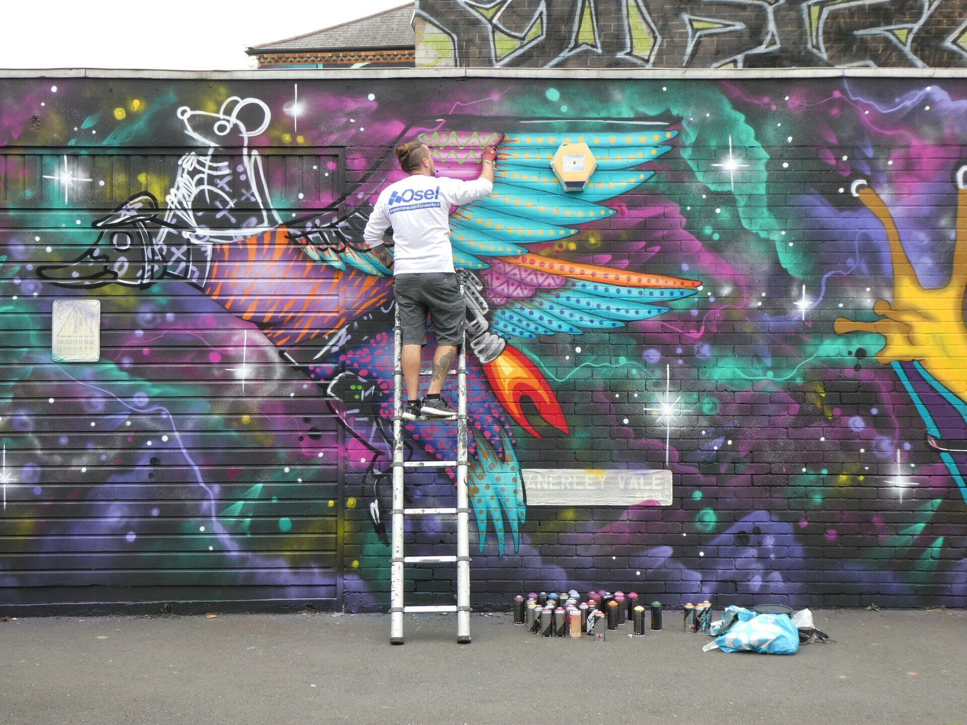 A man on a ladder is painting a mural on a wall.