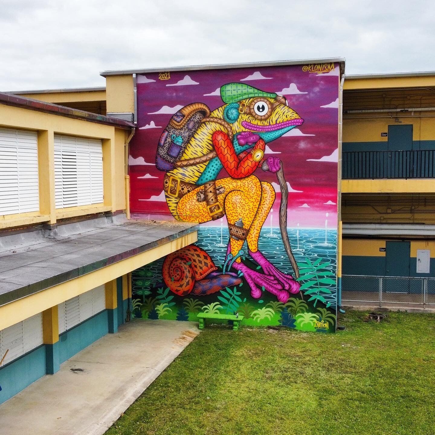 A large mural of a chameleon with a backpack and a cane on the side of a building.